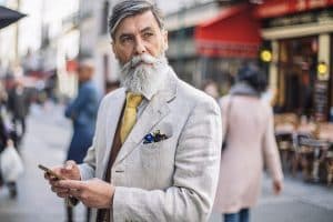 Older bearded male looking off into the distance with a cellphone in his hand