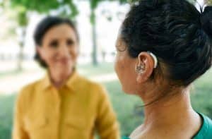 Adult woman with a hearing impairment uses a hearing aid to communicate with her female friend at city park. Hearing solutions Adult woman with a hearing impairment uses a hearing aid to communicate with her female friend at city park. Hearing solutions
