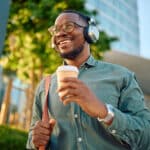 Smiling man wearing headphones and holding a coffee.