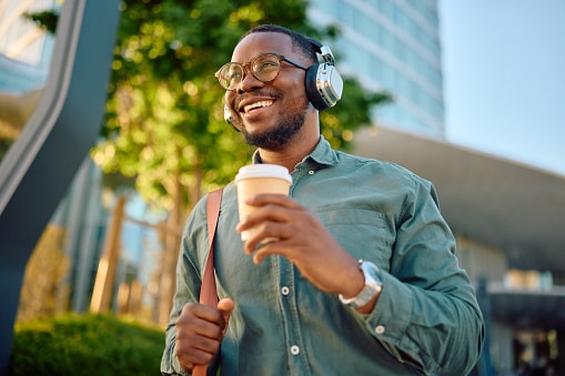 Smiling man wearing headphones and holding a coffee.