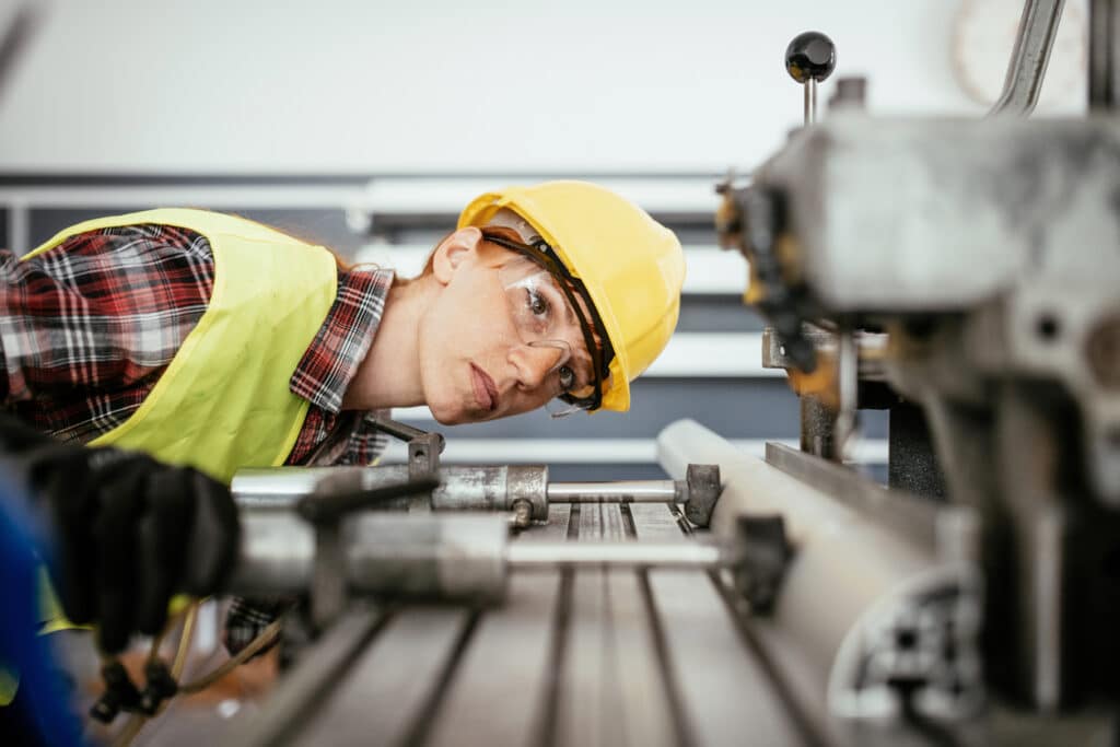 Woman with protective equipment working on the drill in factory plant.
