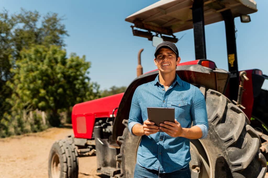 Farmer standing in from of a tractor holding a tablet.