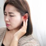 Woman holding her sore, red ear.