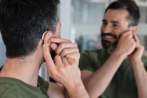 Happy man putting on his hearing aid.