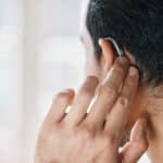 Man touching his behind-the-ear hearing aid.
