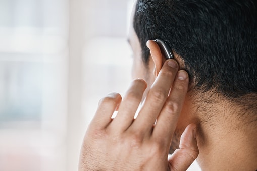 Man touching his behind-the-ear hearing aid.