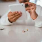 Hearing aid sitting on a table; a man using his tablet in the background.