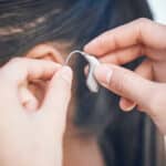 Hands holding a hearing aid up to a patient's ear.