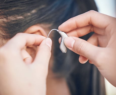 Hands holding a hearing aid up to a patient's ear.