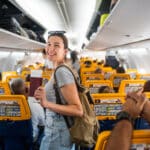 Young woman passenger feeling happy and excited while traveling by airplane, holding passport and boarding pass, ready for vacation