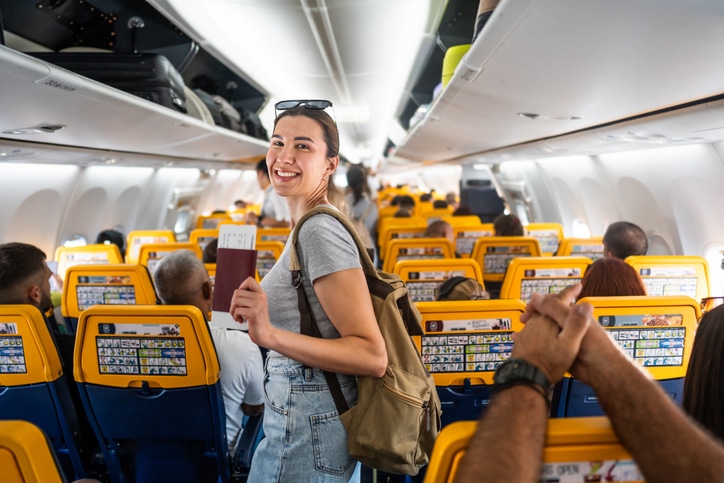 Young woman passenger feeling happy and excited while traveling by airplane, holding passport and boarding pass, ready for vacation.